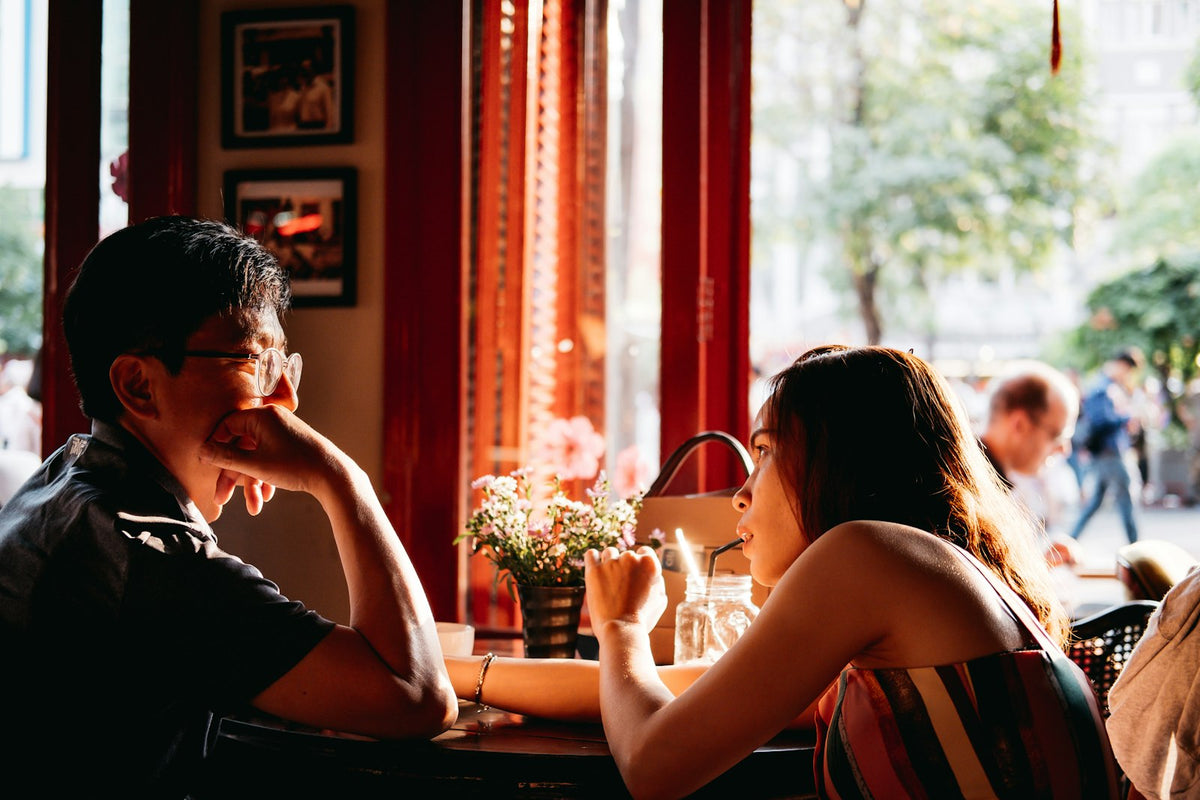 Homem de camisa preta à mesa com uma mulher, roupa para primeiro encontro masculino